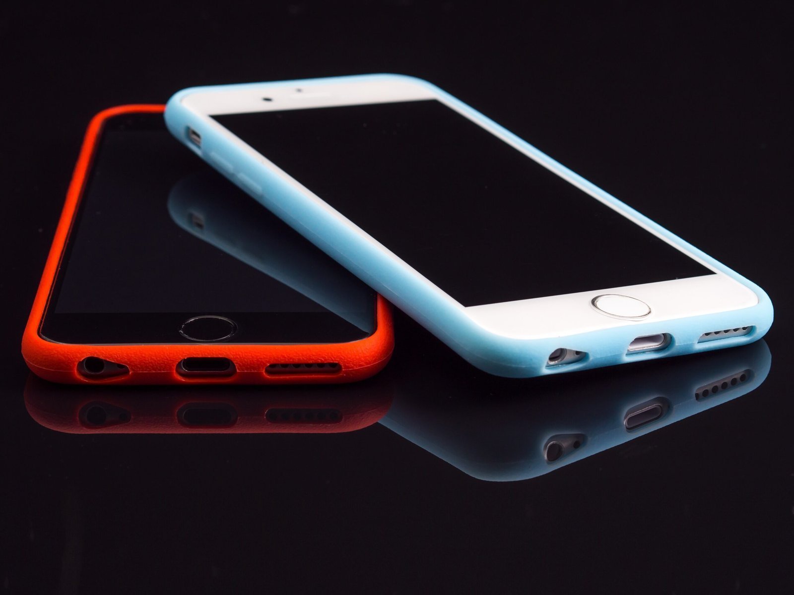 Zwei Smartphones in Schutzhüllen, eines rot, eines hellblau, liegen auf einer dunklen Oberfläche.