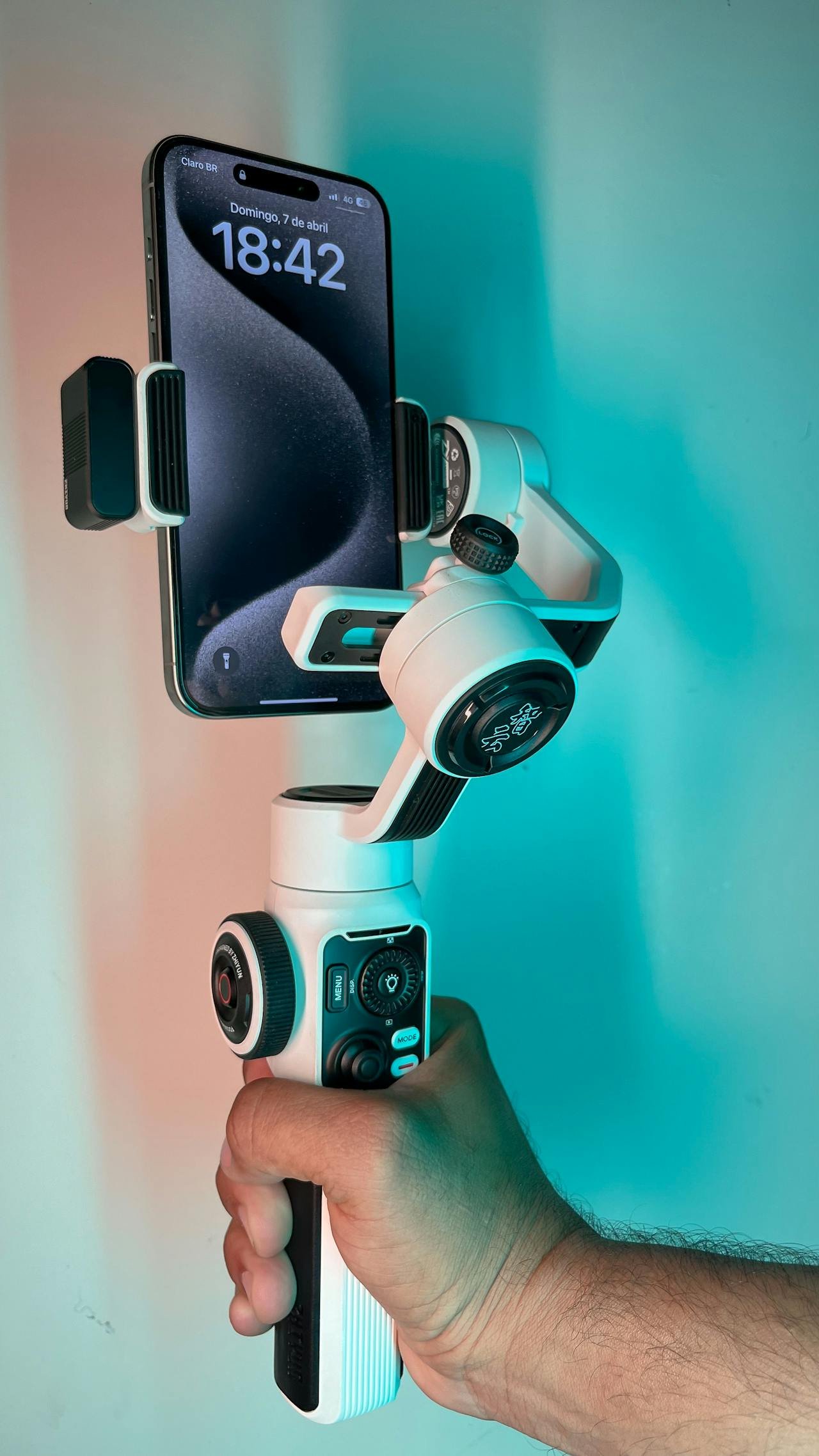 Person hält Smartphone in einem weißen Gimbal-Stabilisator. Das Telefon zeigt die Uhrzeit 18:42 an.
