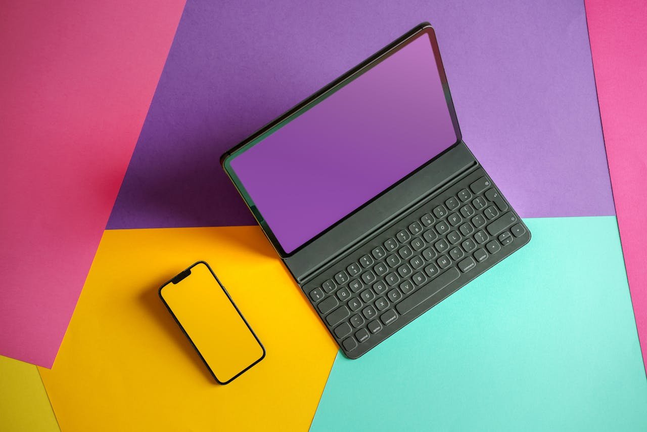 Schwarzes Tablet mit Tastatur und gelbes Smartphone auf buntem Hintergrund. Gadget-FAQs.