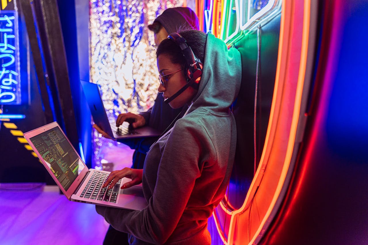 Zwei Hacker arbeiten in einem neonbeleuchteten Raum an Laptops.