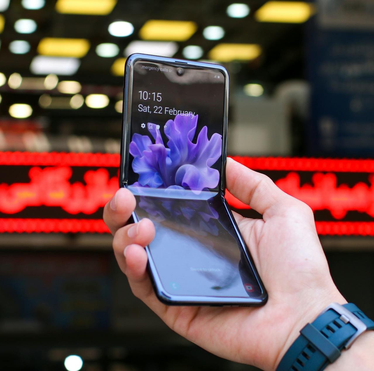 Person hält ein geöffnetes Samsung Galaxy Z Flip-Telefon, auf dem Uhrzeit und Datum angezeigt werden.